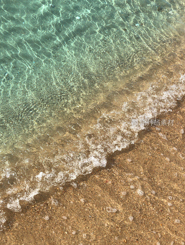 夏日的海滩，清澈平静的海浪拍打着海岸和金色的沙滩，蓝绿色的水反射着蓝天和涟漪，海滩度假，海浪泡沫/泡沫从潮汐和潮湿的沙子在阳光明媚的日子